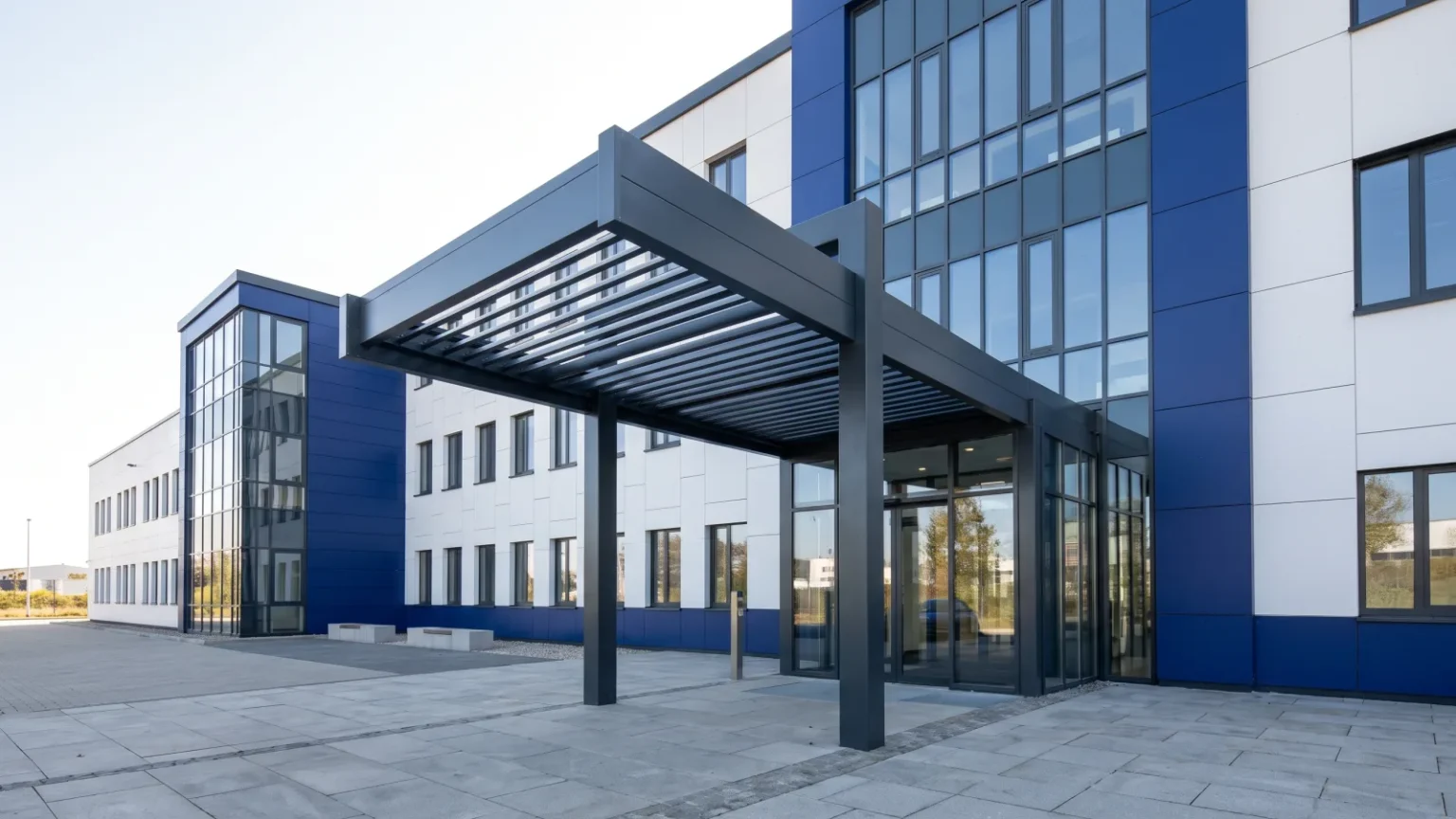Moderne Metallbau Überdachung als Eingangsbereich eines Gewerbegebäudes mit blauer Fassade.